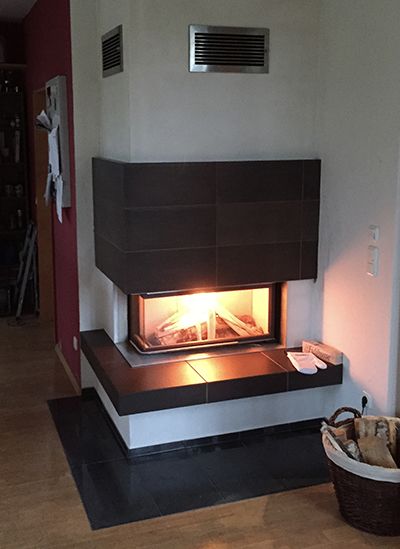 Heizkamin mit dunkler Verkleidung, darunter eine Bank mit Holzfach
